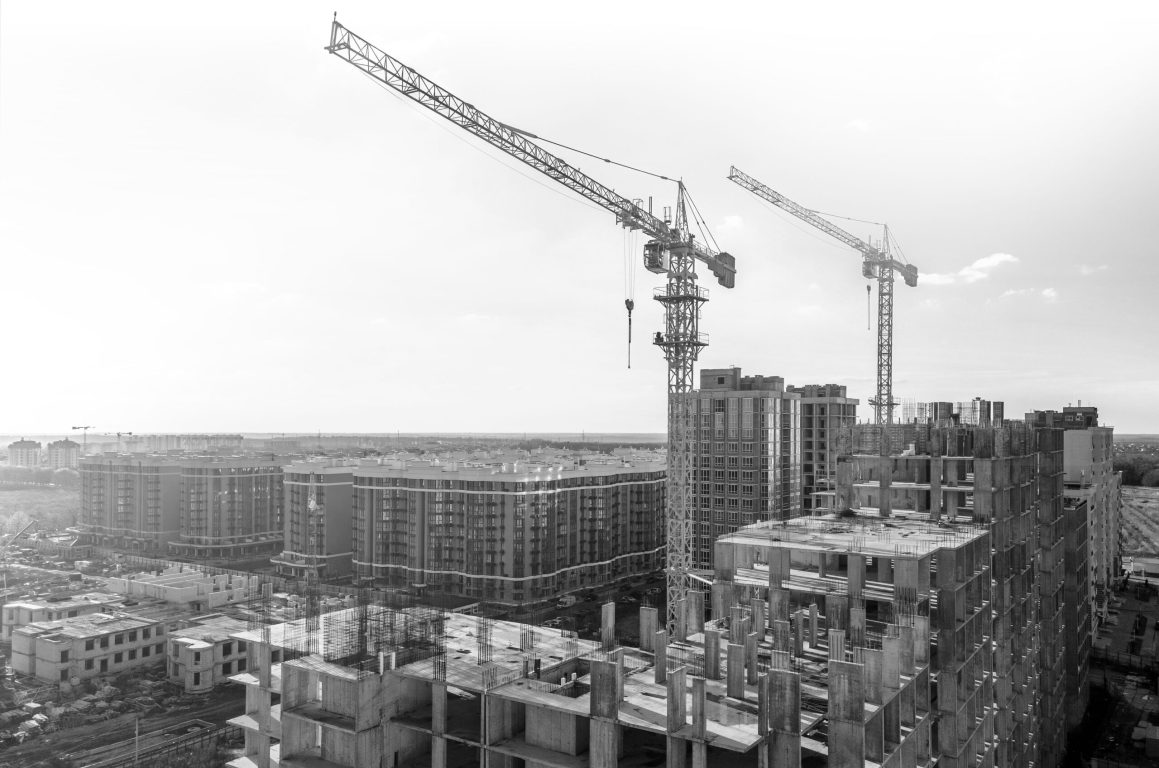 Cranes on the construction site surrounded by new real estates. Scenic aerial photo of growing city districts